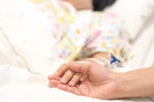 A parent holds their child's hand during palliative care at Ryan House